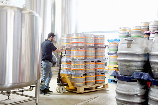 Travailleur dans une brasserie organisant des tonneaux de bière pour la livraison — Photo de stock