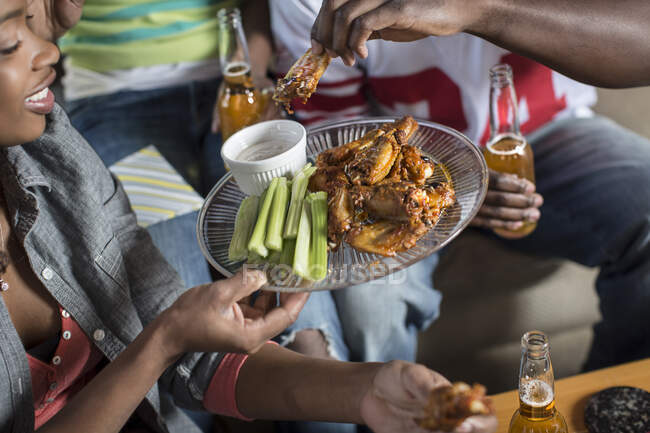 Amici che festeggiano guardando e facendo il tifo per gli sport in TV e mangiando ali di pollo — Foto stock
