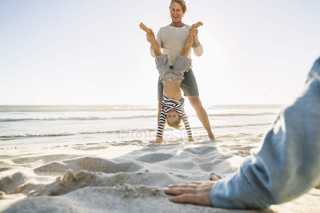 Padre en la playa ayudando hijo haciendo handstand - foto de stock