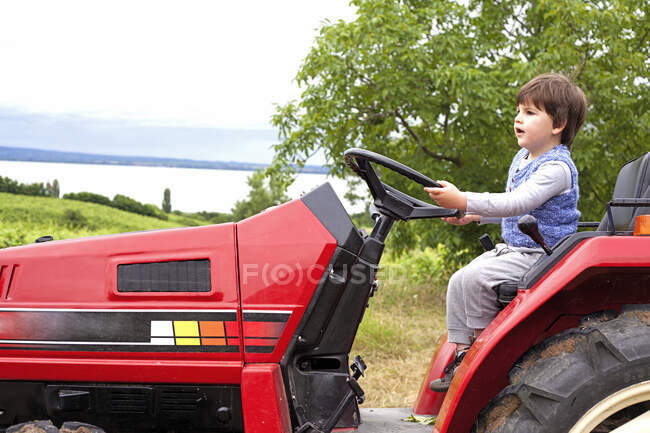 Male toddler pretending to drive tractor in garden — Stock Photo