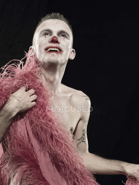 Studio portrait of young man in clown face paint with pink feather boa — Stock Photo