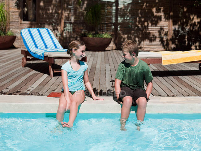 Boy and girl on edge of swimming pool — Stock Photo