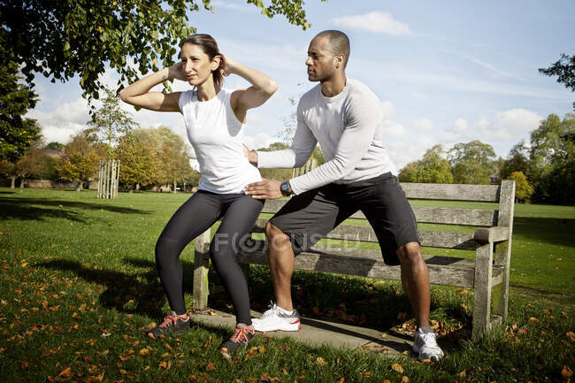 Homme guidant femme faisant squats dans le parc — Photo de stock