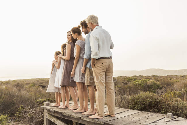Rear view of two girls and family adults standing in height order on boardwalk, Grotto Bay, South Africa — стоковое фото
