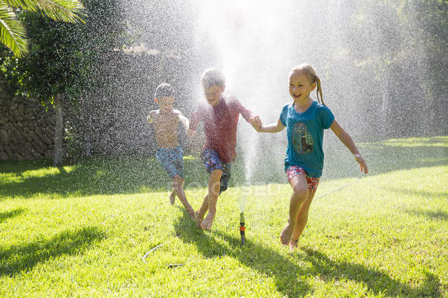 Три дитини в саду біжать крізь воду спринклер — стокове фото
