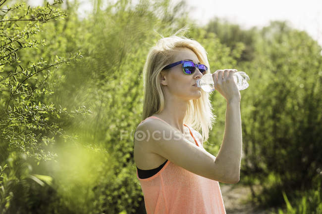 Молода жінка в парку п'є пляшку води — стокове фото