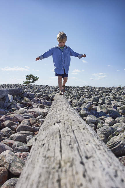 Мальчик балансирует на бревне на пляже — стоковое фото