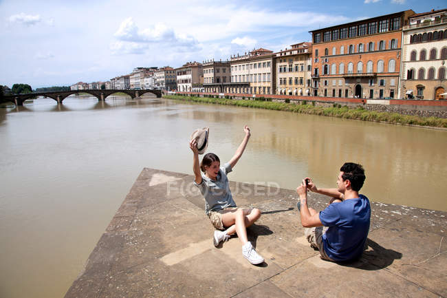 Hombre fotografiando mujer con Ponte alle Grazie en el fondo, Florencia, Toscana, Italia - foto de stock