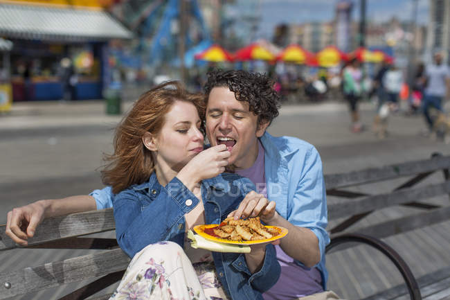 Pareja romántica comiendo patatas fritas en el parque de atracciones - foto de stock