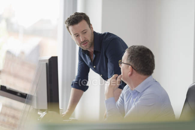 Dos trabajadores de oficina hablando mientras trabajan en la oficina en el escritorio con monitor de computadora - foto de stock