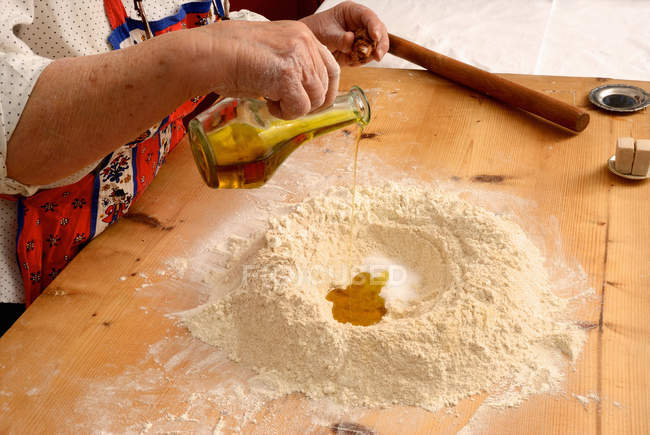 Cropped image of senior woman pouring olive oil in flour in kitchen — Stock Photo