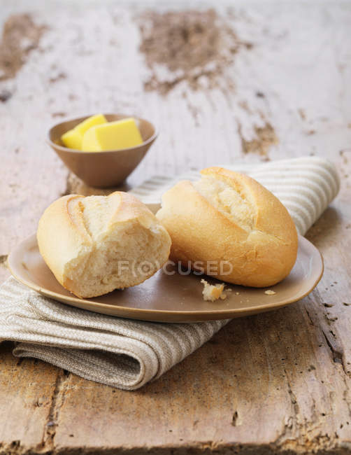 Halved white petit pain with butter on ceramic plate and striped napkin — Stock Photo