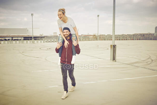Homem adulto médio dando passeio de ombro para namorada no estacionamento no telhado — Fotografia de Stock