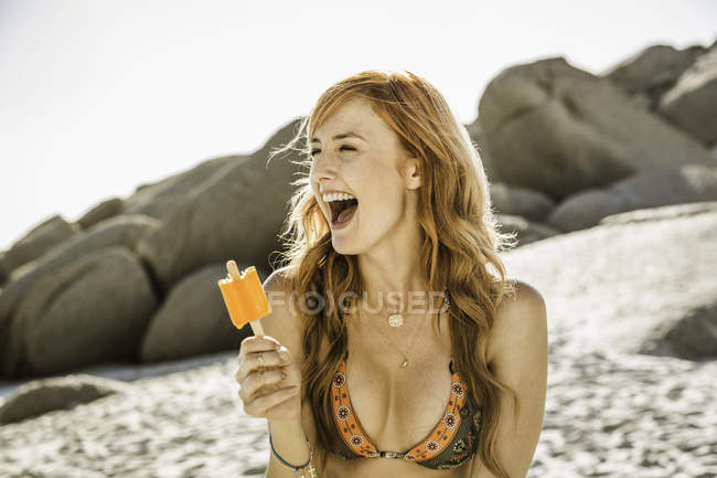 Laughing woman with long red hair eating ice lolly on beach, Cape Town, South Africa — Stock Photo