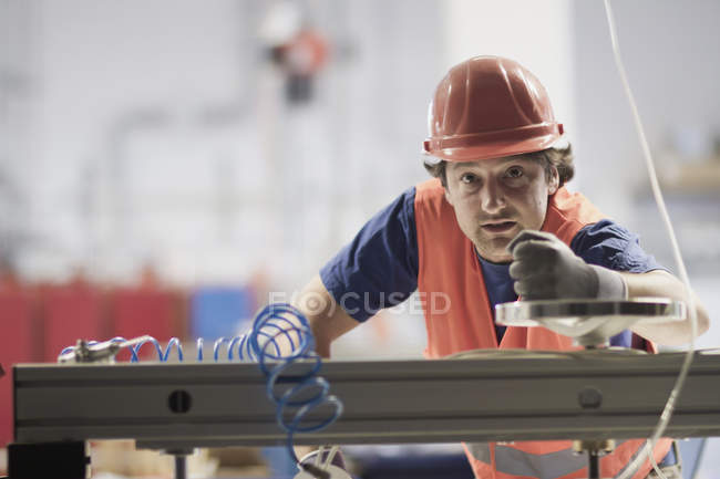 Homem adulto médio usando chapéu duro olhando para a câmera, máquina de operação — Fotografia de Stock