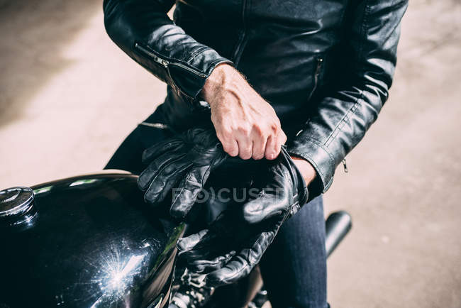 Mid section of male motorcyclist sitting on motorcycle putting on gloves — Stock Photo