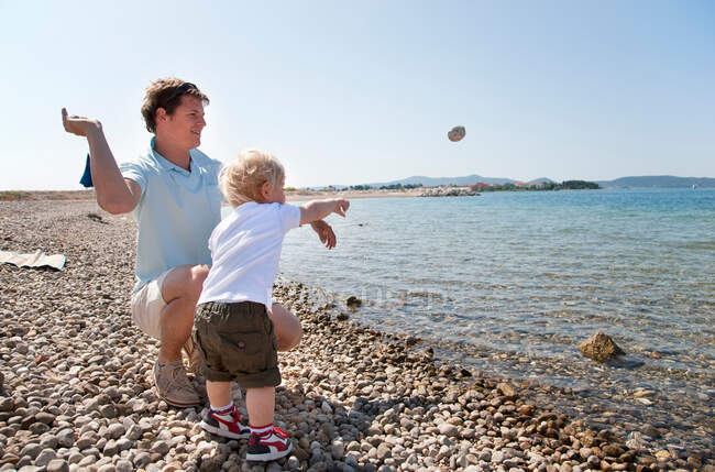 Padre e figlio gettano sassi sulla spiaggia — Foto stock