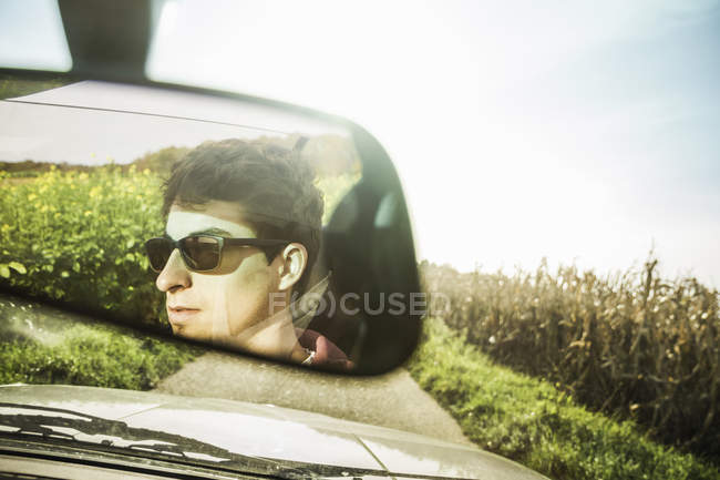 Mirror reflection of young man driving on country road — Stock Photo