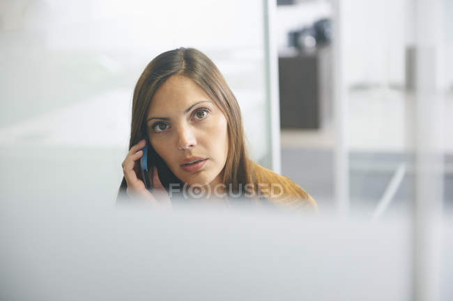 Mulher usando smartphone e olhando na câmera no escritório moderno — Fotografia de Stock