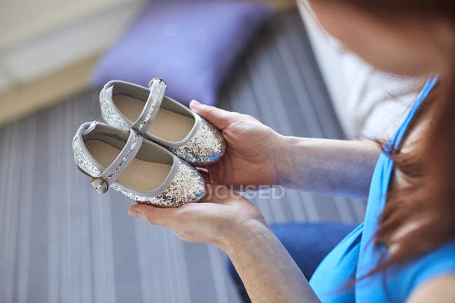 Over shoulder view of pregnant woman holding silver shoes — Stock Photo