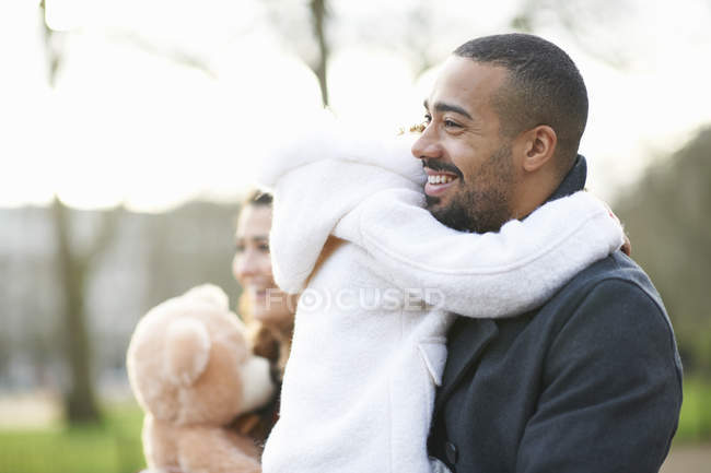 Vista lateral de pai sorrindo carregando filha — Fotografia de Stock