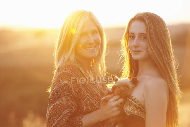 Donna e adolescente in piedi in campo al crepuscolo tenendo cane domestico — Foto stock