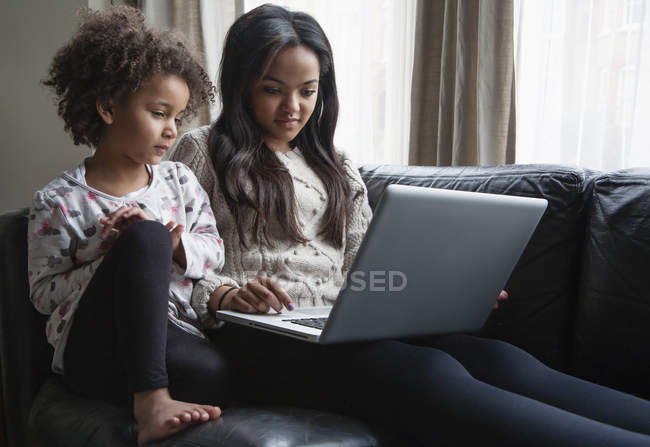 Дві сестри сидять на дивані і використовують ноутбук — стокове фото