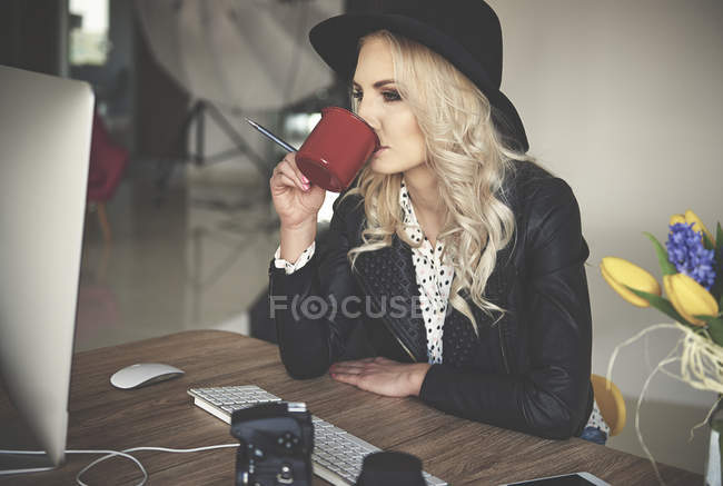 Photographer looking at photography studio computer while drinking coffee — Stock Photo