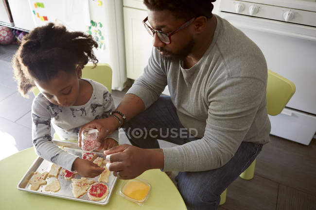 Отец и дочь украшают невыпеченные печенья — стоковое фото
