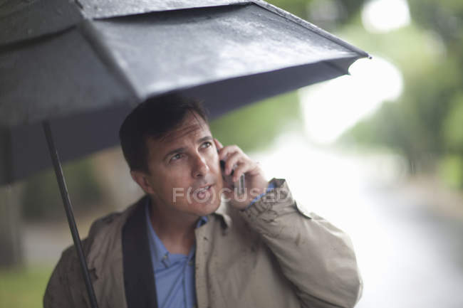 Businessman talking on cellphone whilst carrying umbrella — Stock Photo