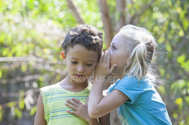 Kleines Mädchen flüstert Junge im Garten zu — Stockfoto