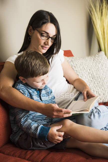 Mãe ensinando filho a ler livro no sofá em casa — Fotografia de Stock