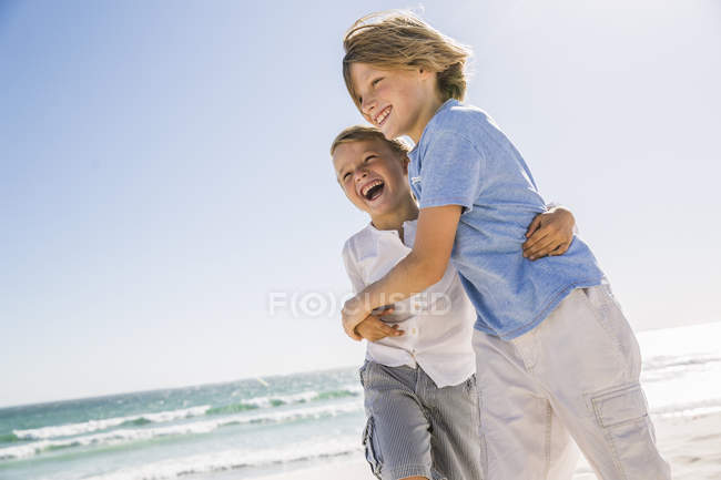 Brothers on beach hugging looking away smiling — Stock Photo
