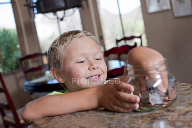 Мальчик кладет сбережения в стеклянную банку — стоковое фото