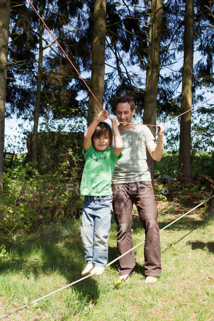Father helping son walk on tight rope — Stock Photo