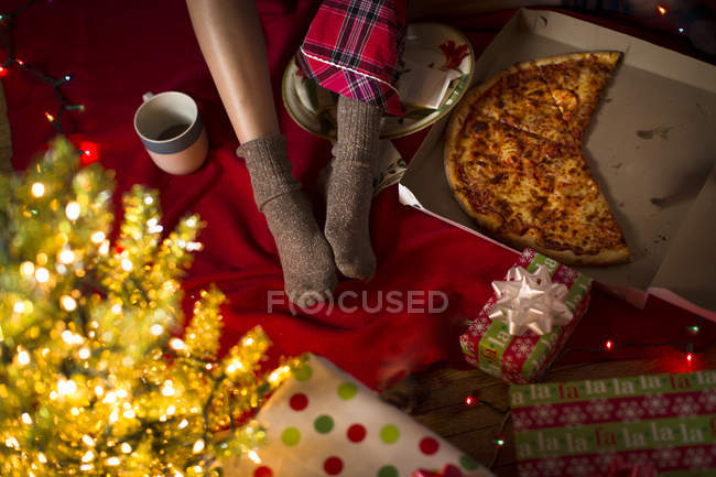 Young woman's legs amongst christmas gifts and pizza box — Stock Photo