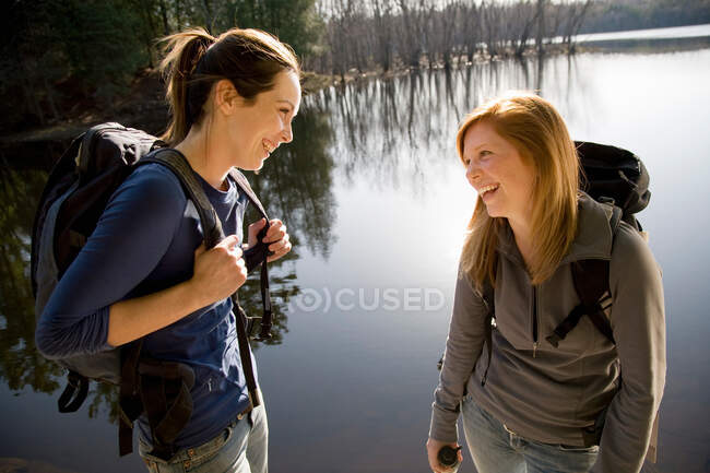 Two women laughing beside lake — Stock Photo