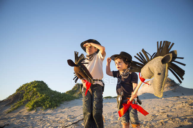 Dois irmãos vestidos de cowboys sombreando os olhos com as mãos — Fotografia de Stock