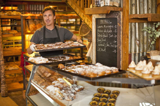 Mature man holding tray of fresh pastries in bakery — Stock Photo