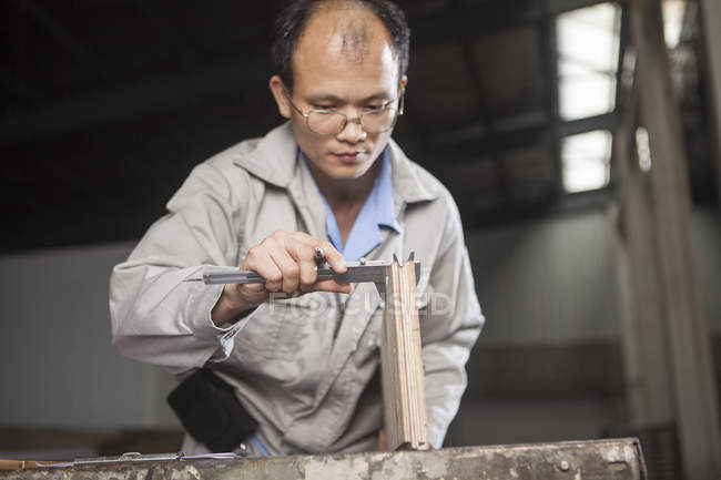 Carpintero midiendo tablón de madera con pinza vernier en fábrica, Jiangsu, China - foto de stock