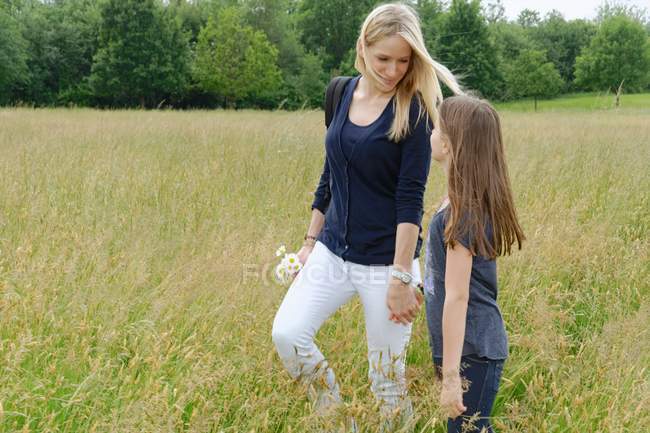 Madre e hija paseando por el campo herboso - foto de stock