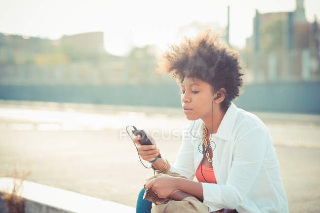 Young woman choosing music on smartphone in city — Stock Photo