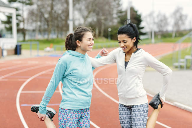 Two young women on running track, exercising, stretching — Stock Photo
