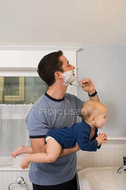 Батько голиться і тримає дитину — стокове фото