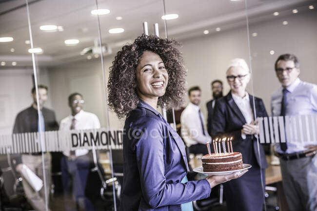 Portrait of young businesswoman carrying celebration cake into boardroom — Stock Photo