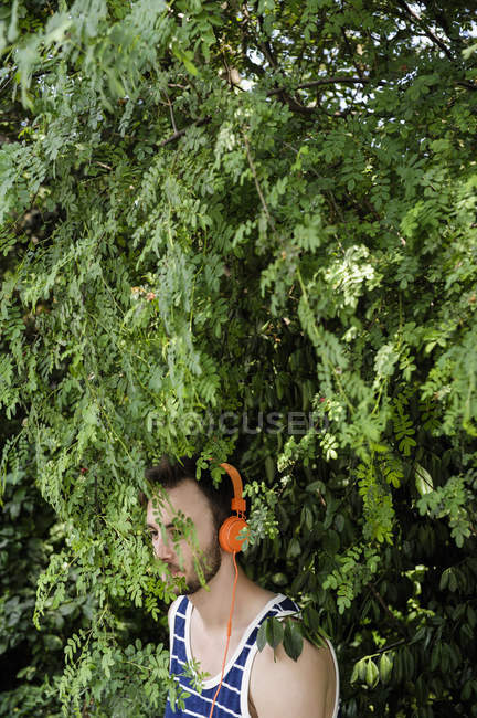 Молодий чоловік у навушниках стоїть у лісистому парку. — стокове фото