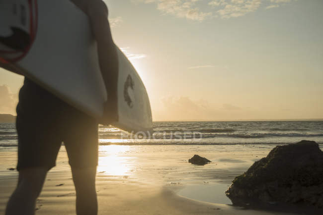 Зрелый человек, идущий к морю, держа доску для серфинга — стоковое фото