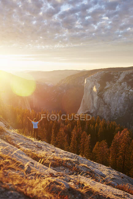 Un excursionista disfruta de la luz del atardecer en Sentinel Dome mientras contempla la majestuosa pared de granito de El Capitán y el valle de Yosemite.. - foto de stock