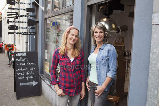 Женщины, стоящие в дверях магазина, смотрят в камеру и улыбаются. — стоковое фото