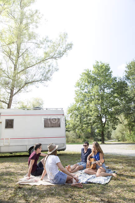Gruppo di giovani adulti seduti su coperta da picnic, relax, camper sullo sfondo — Foto stock